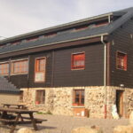 Façade extérieure du refuge de montagne dans les Vosges, avec sa terrasse aménagée de tables en bois pour l'accueil des traileurs.